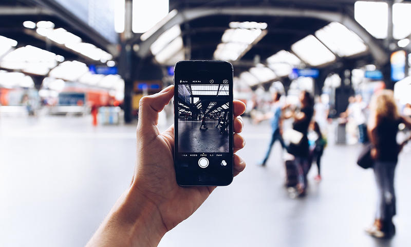 a hand holding a cell phone filming a blurred scene at an airport. Photo by Oleg Magni on Pexels.