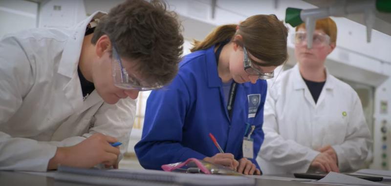 A woman and two men in a chemistry lab making notes 